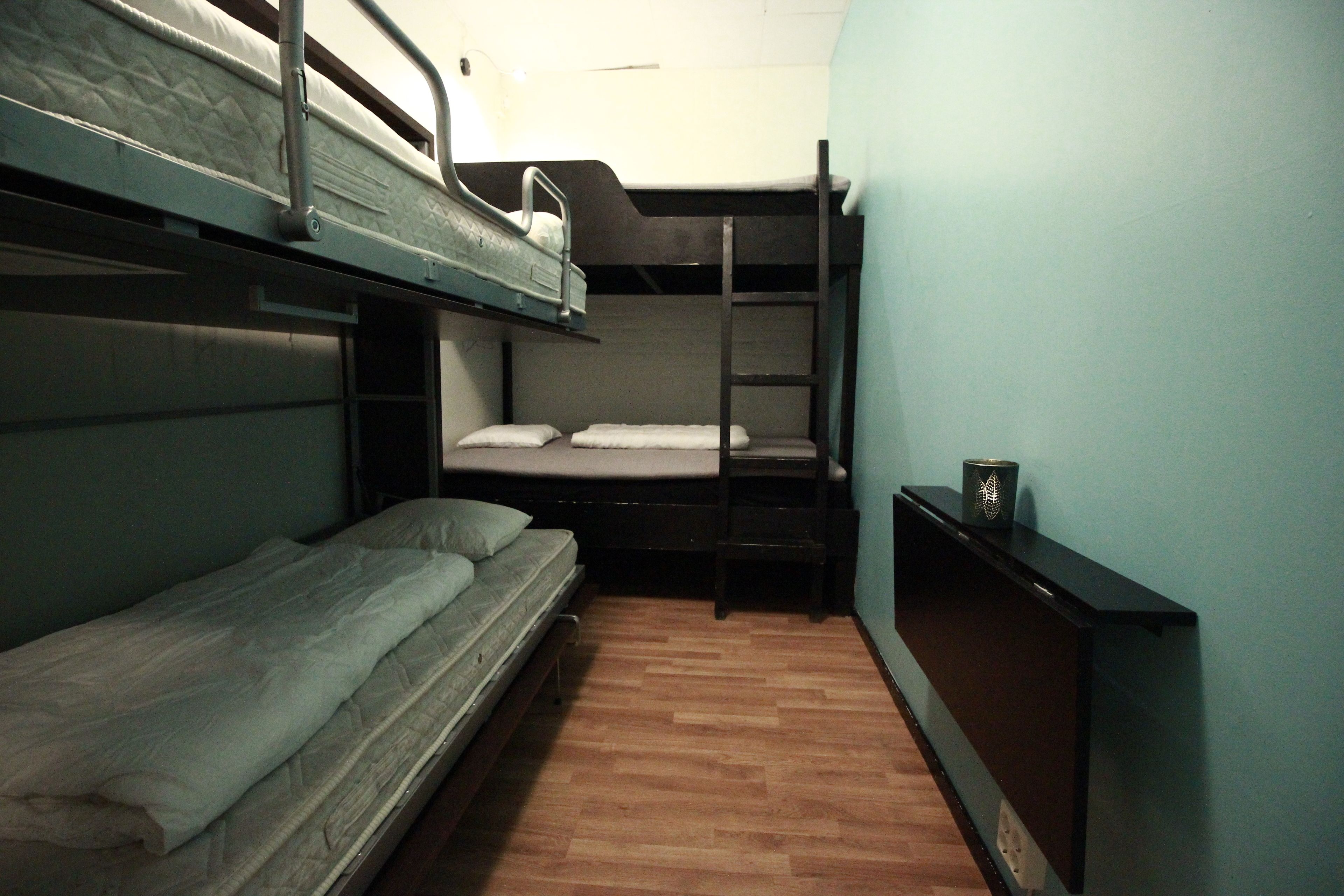 Une chambre de dortoir avec des lits superposés, un plancher en bois et une petite étagère sur laquelle est posé un objet décoratif.