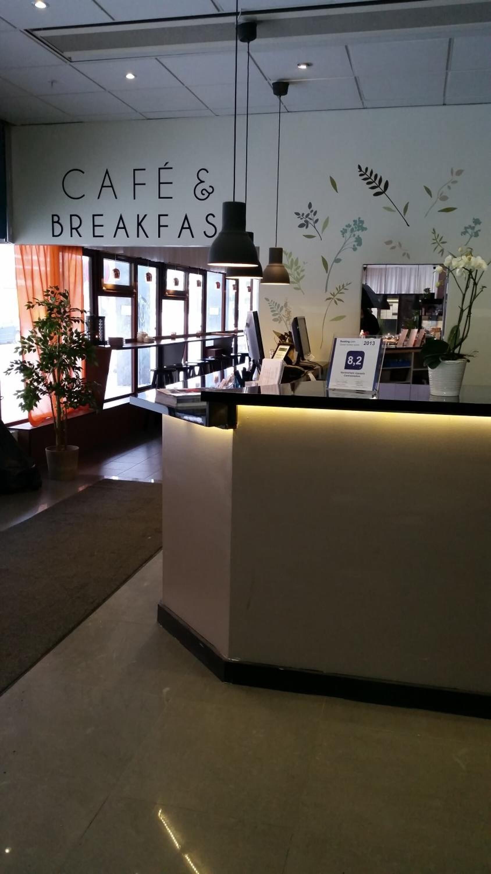 Un área de café y desayuno con una recepción, lámparas colgantes y una pared decorada con motivos florales.
