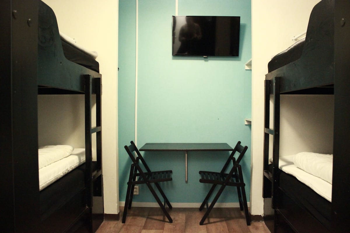 Dormitorio con literas, televisión montada en la pared y un escritorio con dos sillas.