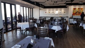 Un restaurante con varias mesas, sillas y vistas amplias por los grandes ventanales.