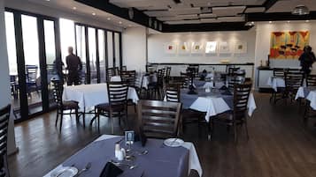 A restaurant with multiple tables, chairs, and a view through large windows.