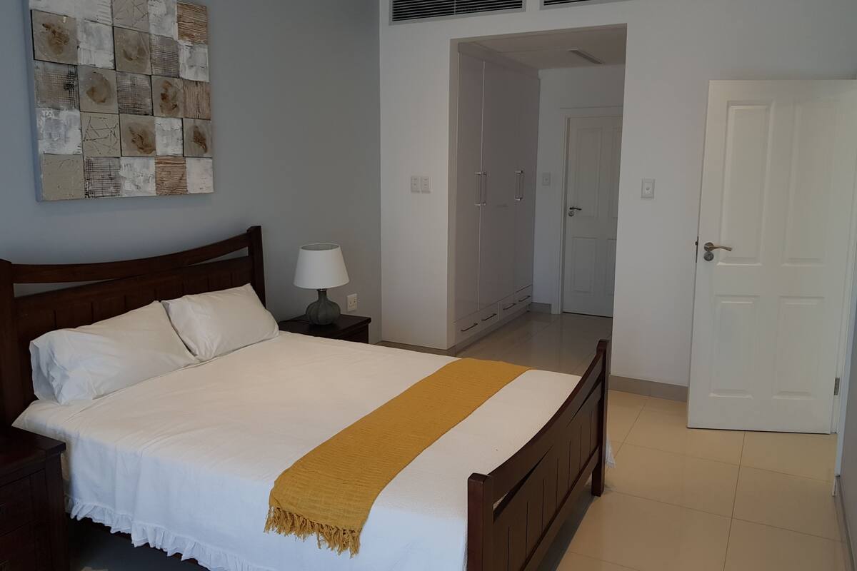 A bedroom with a bed, a nightstand, a lamp, a wardrobe, and a door.
