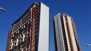 Un moderno edificio de gran altura con una mezcla de estilos arquitectónicos, incluyendo una fachada blanca destacada y un exterior con patrones anaranjados y beige.