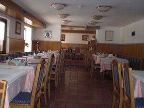 Un restaurante con cabinas y mesas de madera, piso de baldosas y ventiladores de techo.