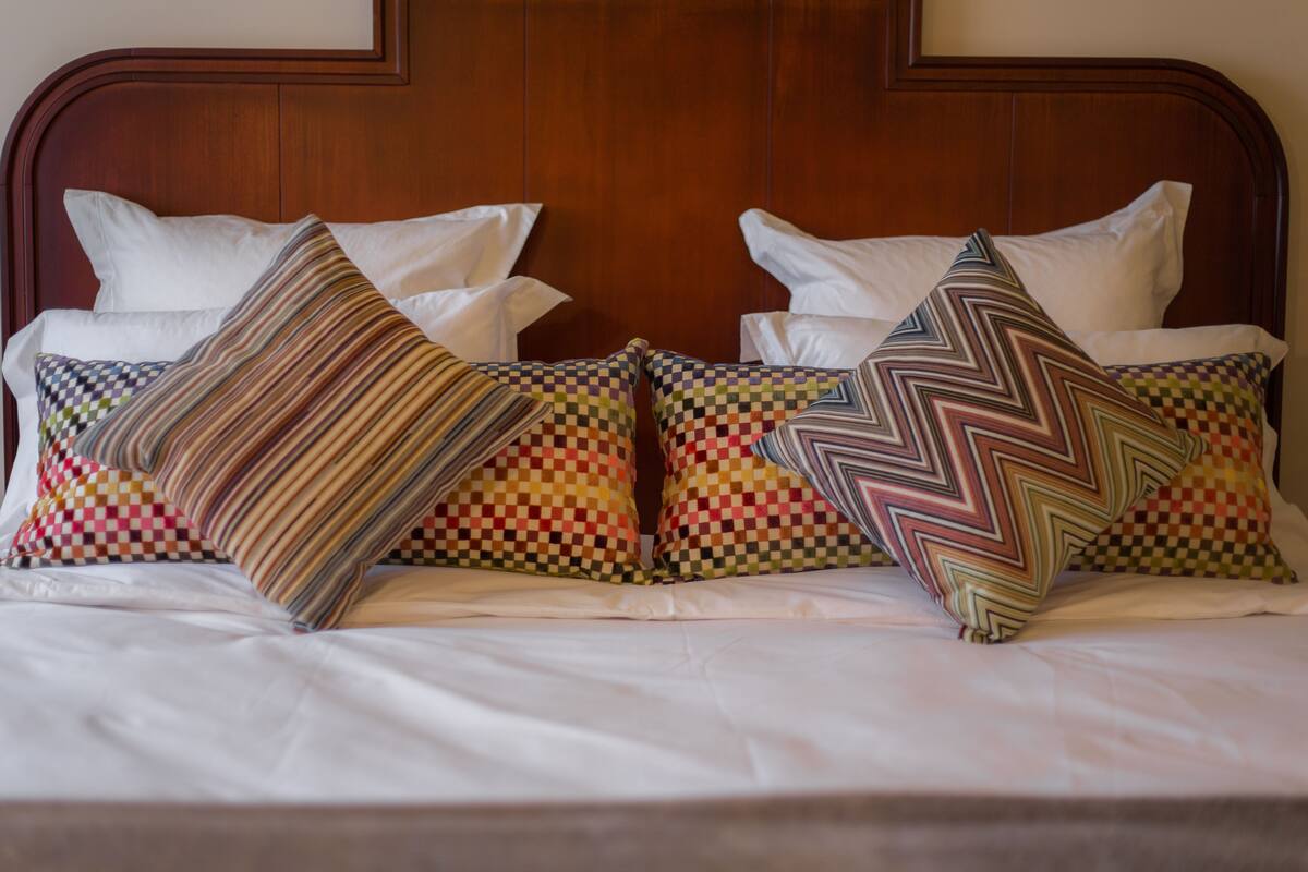 Una cama con cabecera de madera, ropa de cama blanca y almohadas estampadas.
