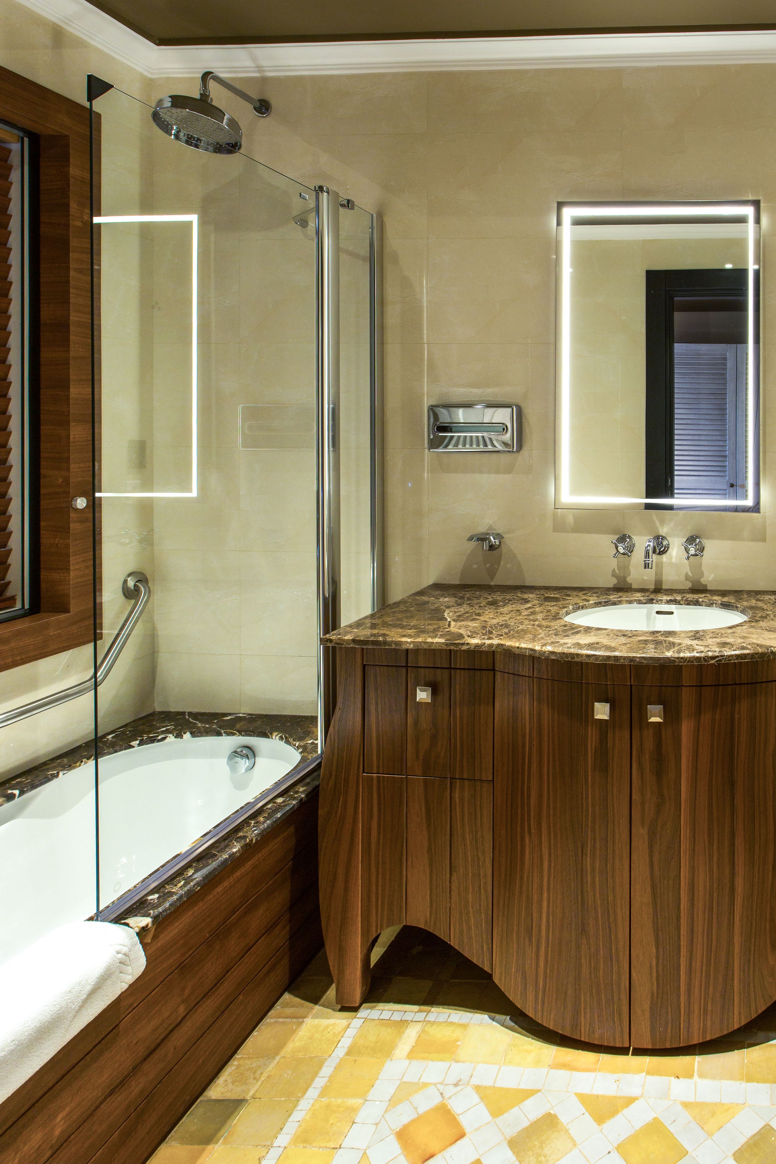 Un baño con cabina de ducha de vidrio, tocador de madera con encimera de mármol y un espejo grande sobre el lavabo.
