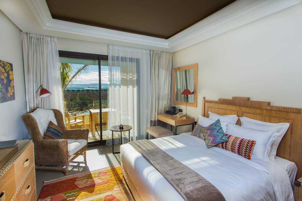 Habitación de hotel con una cama grande, una silla, un escritorio y vistas al exterior.