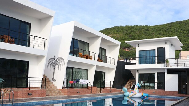 Um hotel moderno com piscina, várias varandas e vista para uma encosta verde.