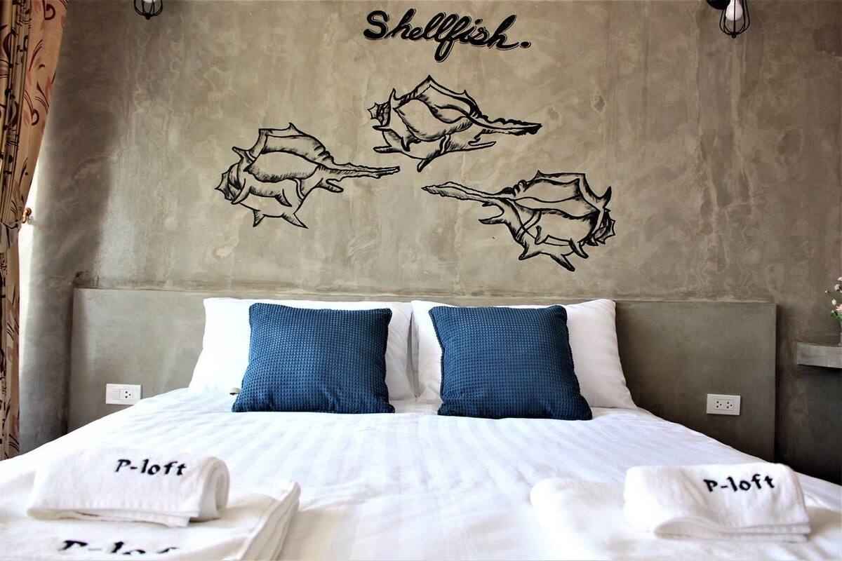 A hotel room with a bed, two blue pillows, and a wall with a shellfish decal.