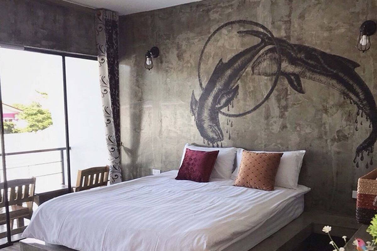 A bedroom with a large bed, a view through a window, and a wall mural.
