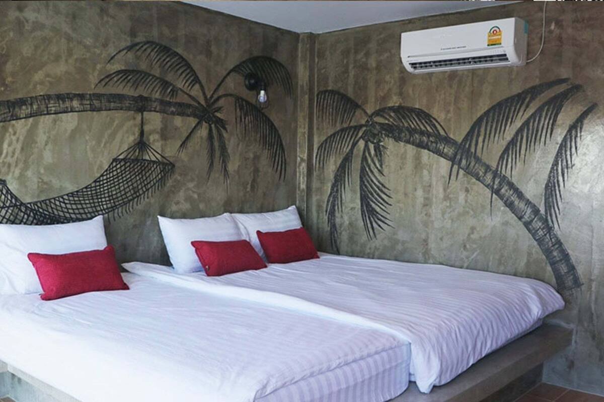 A room with a bed, two red pillows, a hanging hammock, and an air conditioning unit on the wall.