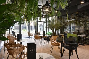 Un restaurante con sillas de mimbre, mesas, plantas colgantes y una estantería para vinos al fondo.