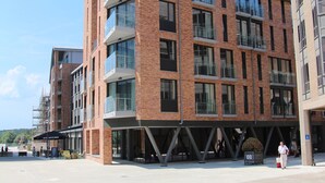 Un immeuble moderne à plusieurs étages, doté d’une façade en briques, de grandes fenêtres et de balcons.