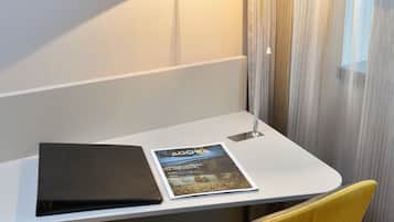 A hotel room with a desk, a lamp, a magazine, and a chair.