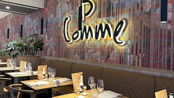 Een restaurantinterieur met gedekte tafels, een muur met een 'B' logo en een decoratief patroon op de muur.