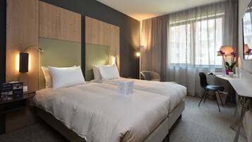 A modern hotel room with a large bed, a desk, and a chair. There are two bedside tables with lamps and a small plant on the desk.