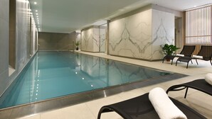 Une piscine avec un sol carrelé, des chaises longues et une plante en pot.