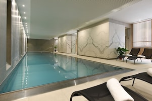 Una piscina con piso de baldosas, sillas de descanso y una planta en maceta.
