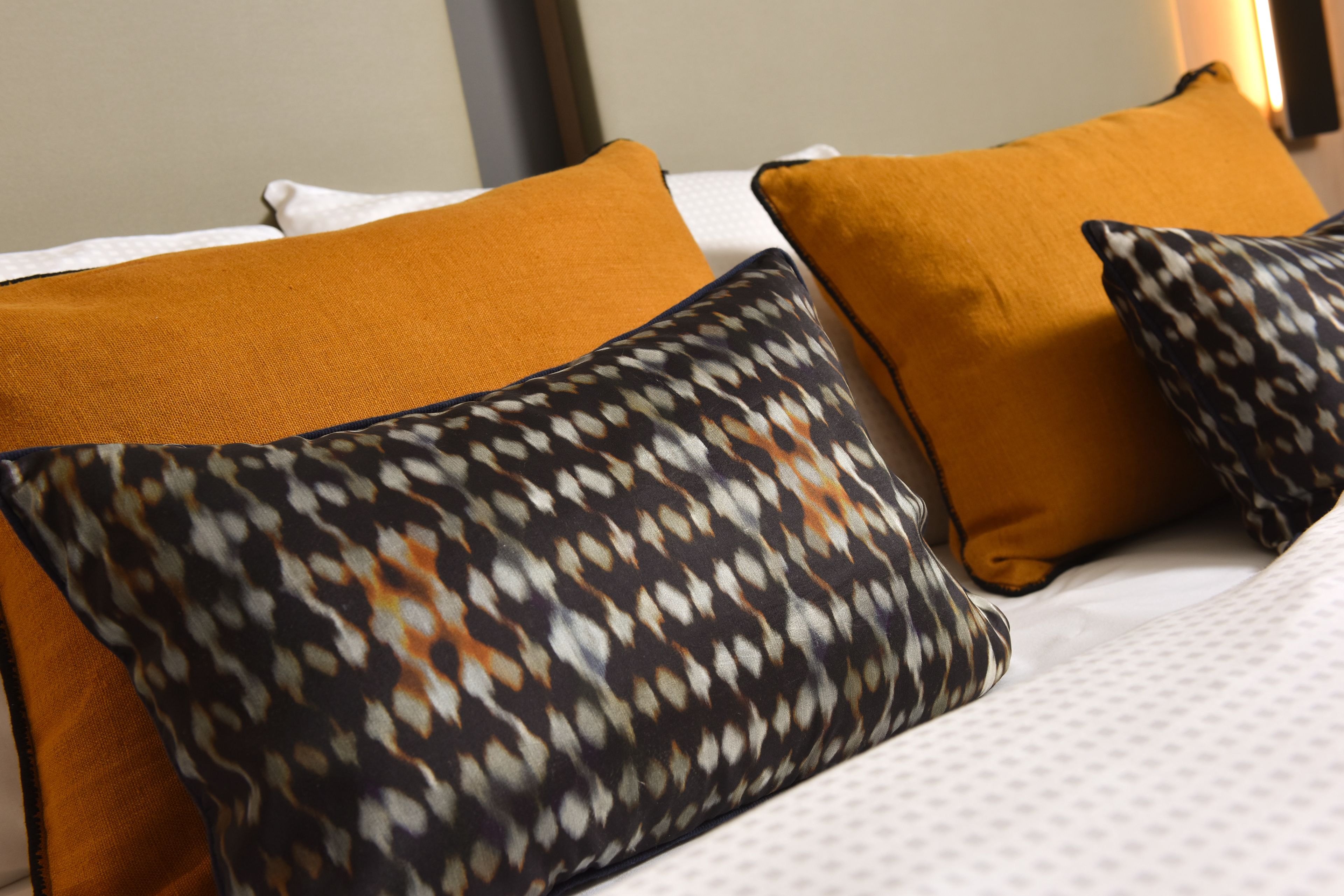 A bed with white bedding and multiple pillows, including a patterned one and two solid-colored ones.