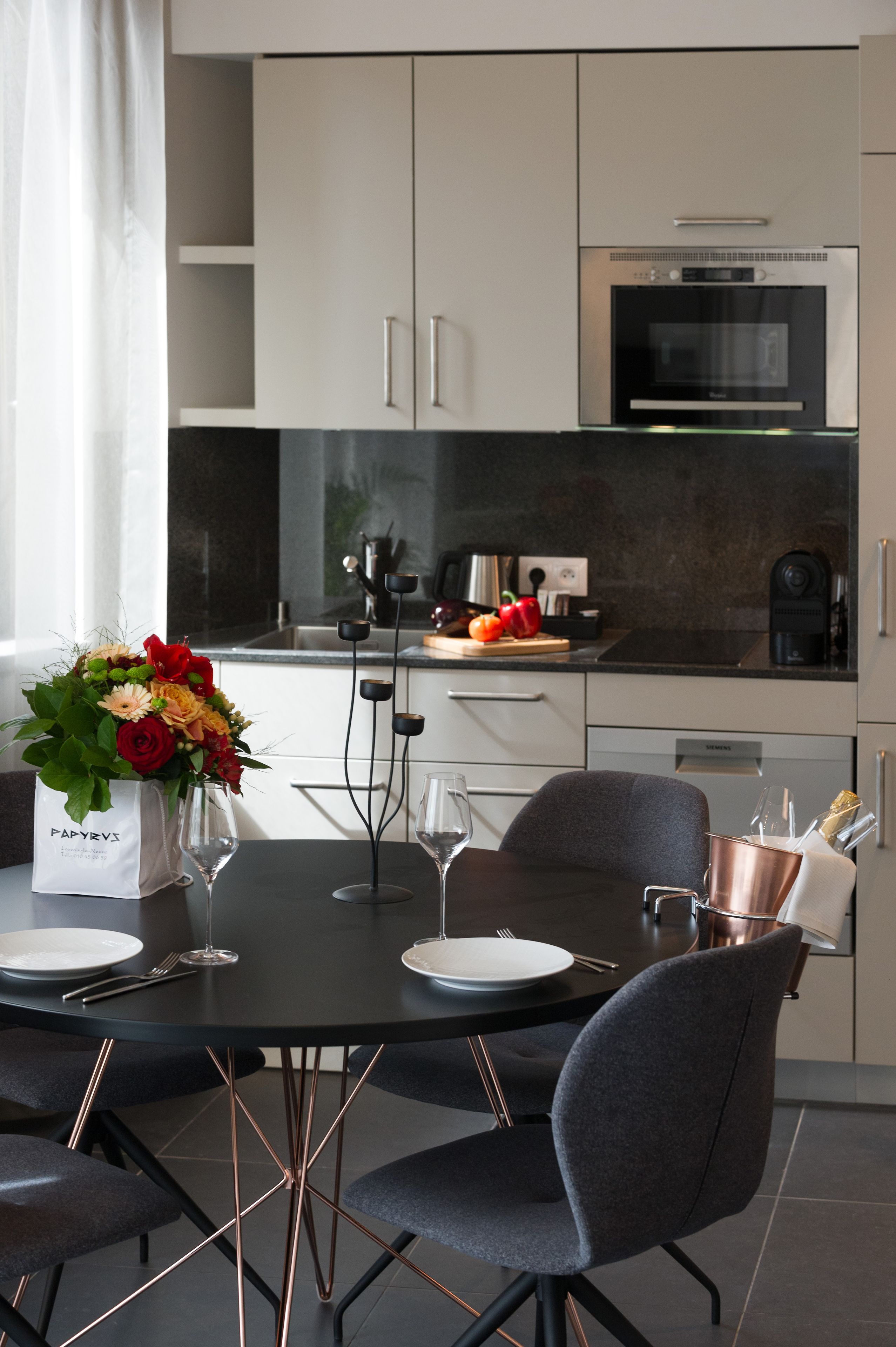 Una cocina moderna con comedor, que presenta un comedor negro, sillas grises y un ramo de flores sobre la mesa.