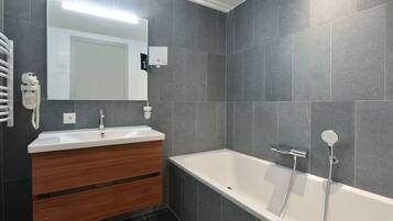 Ein modernes Badezimmer mit einer großen Badewanne, einem Waschtisch mit Spiegel und einem Handtuchhalter.