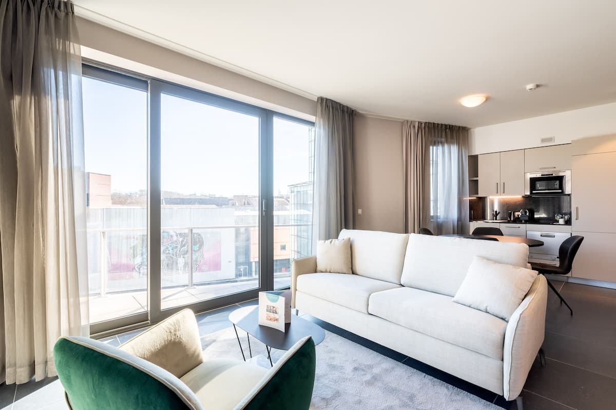 A modern living room with a sofa, a small table, and a view of the city through large windows.