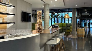 A modern bar area with a long counter, stools, and a large decorative pillar. - Martin's All Suites (Ottignies-Louvain-la-Neuve)