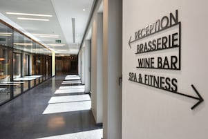 Un pasillo moderno de hotel con señales indicativas para Recepción, Brasserie, Bar de vinos y Spa & Fitness.