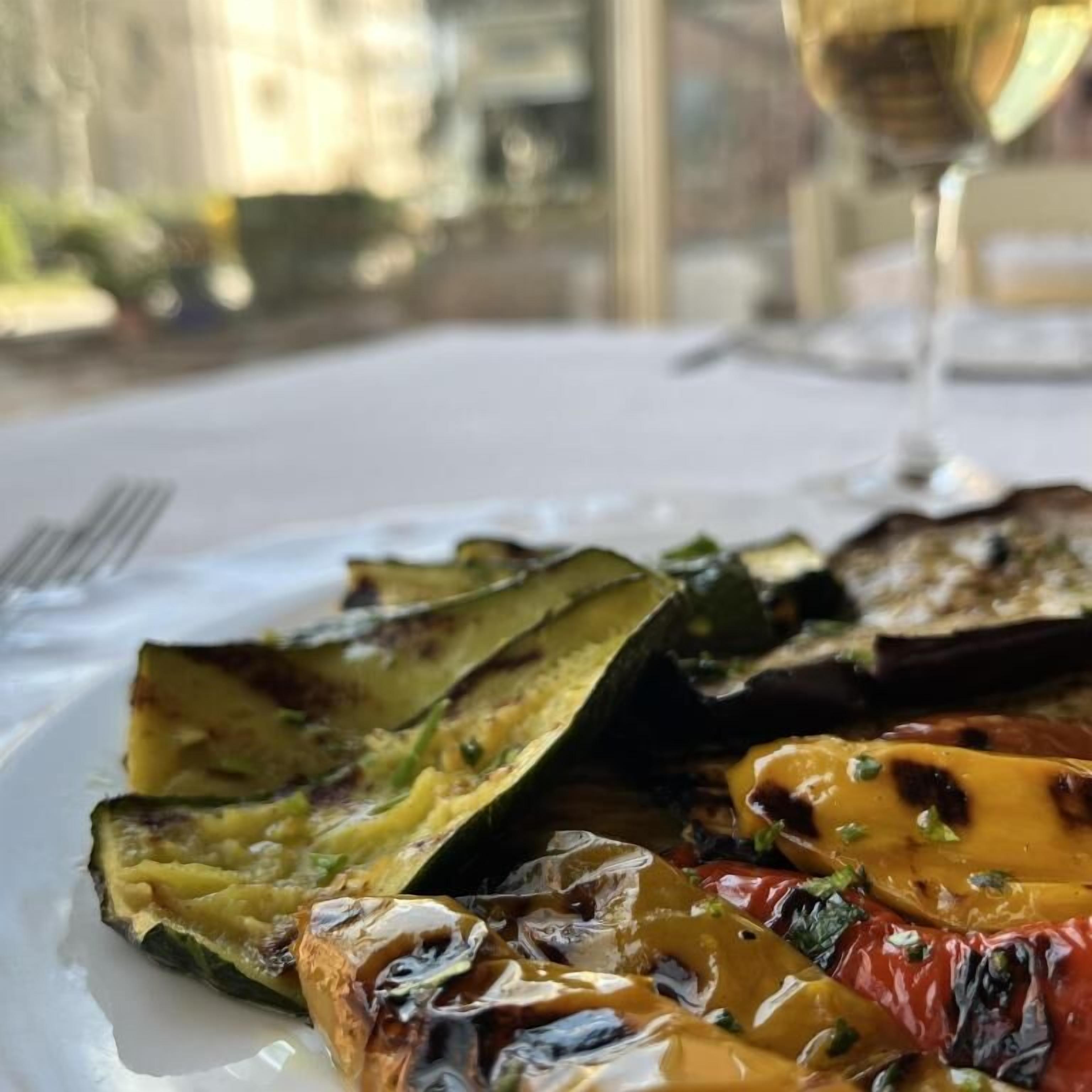 Ein Teller mit gegrilltem Gemüse und ein Glas Wein auf dem Tisch.