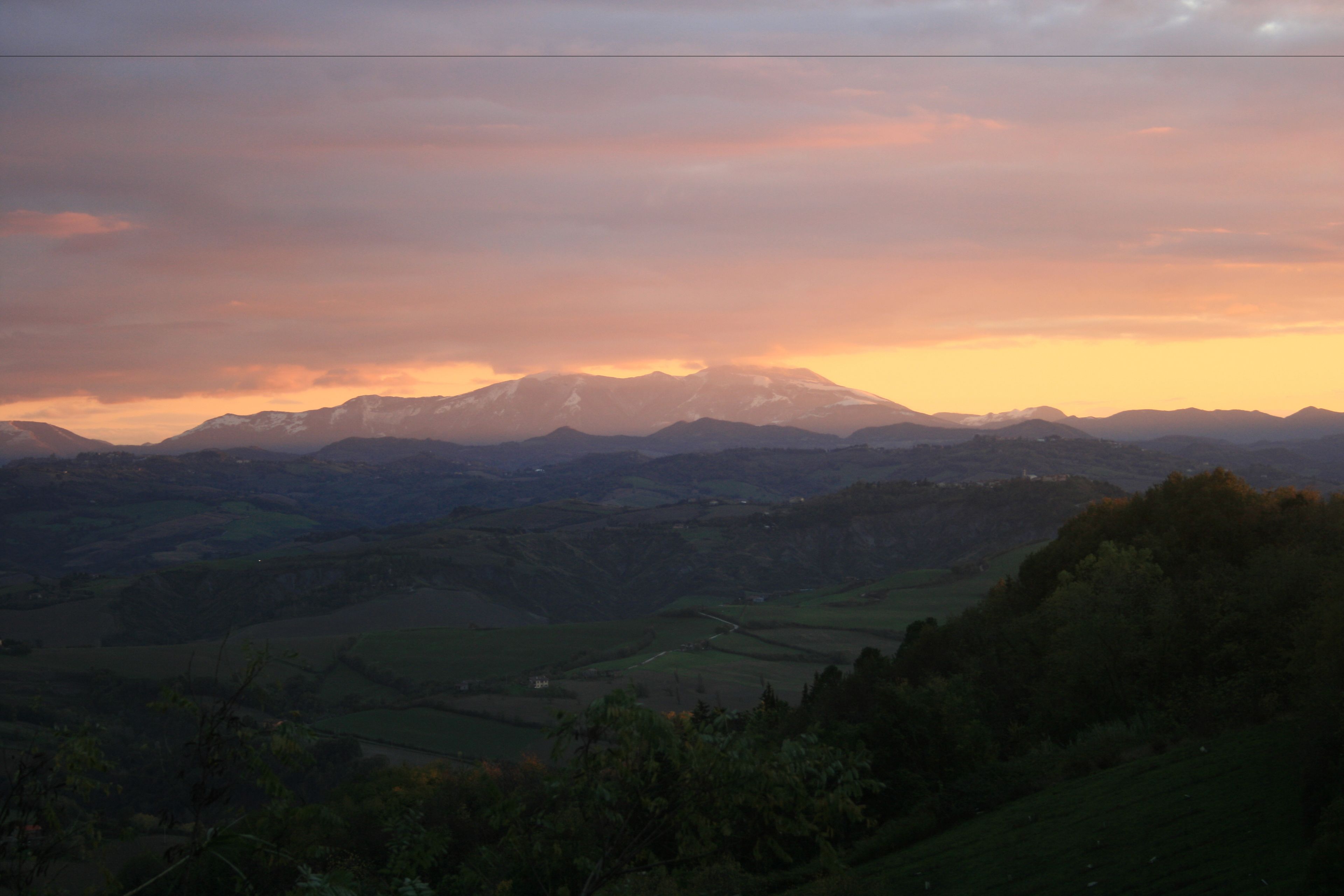 A panoramic view of a mountainous landscape with fields and a distant mountain range.