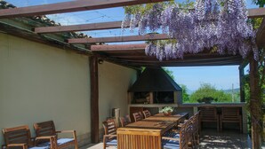 An outdoor patio with a wooden table and chairs, a hanging purple flower arrangement, and a view of greenery in the background. - B&B La Fenice (Mondaino)