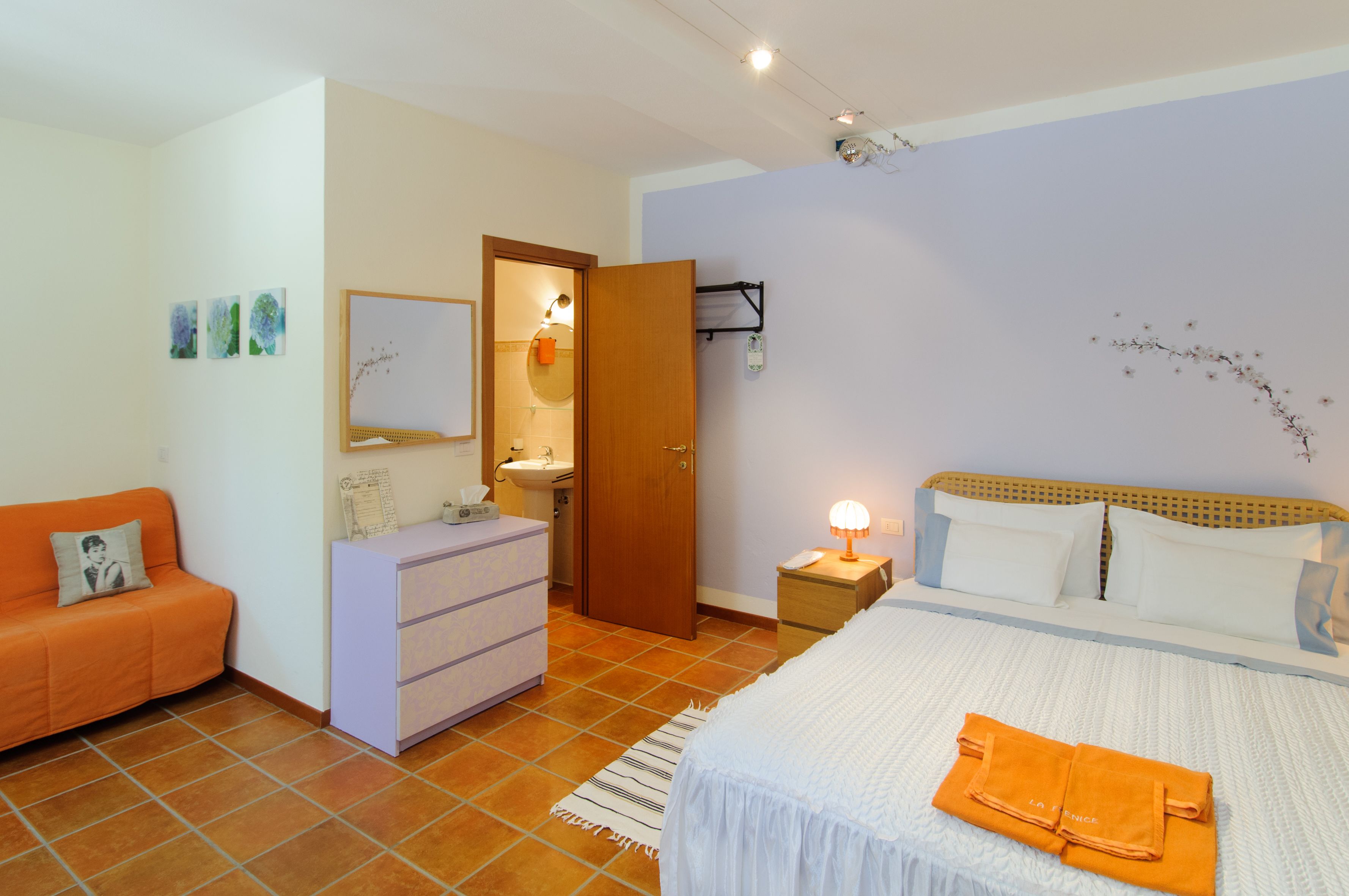 Una camera da letto con un letto, un comodino, una cassettiera, un bagno e un divano.