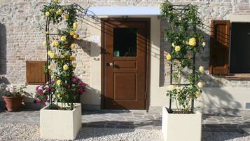 Un bâtiment doté d’une façade en pierre, d’une porte en bois et de deux plantes en pot, dont certaines sont en fleurs.