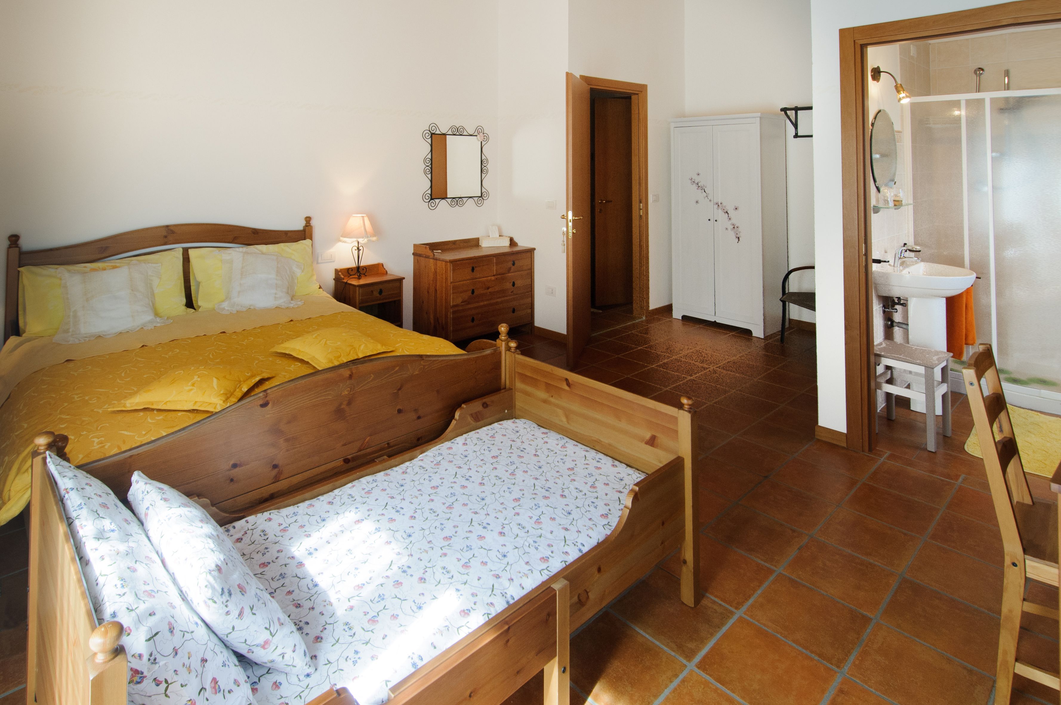 Un dormitorio con una cama de madera, una mesita de noche con lámpara, un aparador y una puerta que da al baño.