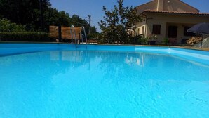A clear blue swimming pool with a wooden deck and metal ladder. - B&B La Fenice (Mondaino)