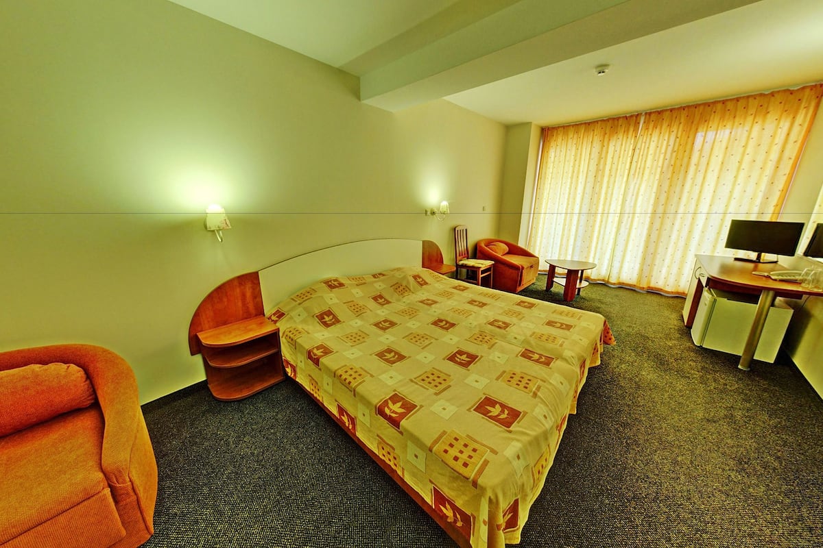 A hotel room with a bed, a desk with a computer, a chair, and a small table.