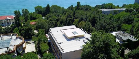 An aerial view of a building complex surrounded by dense greenery, with a body of water in the background.