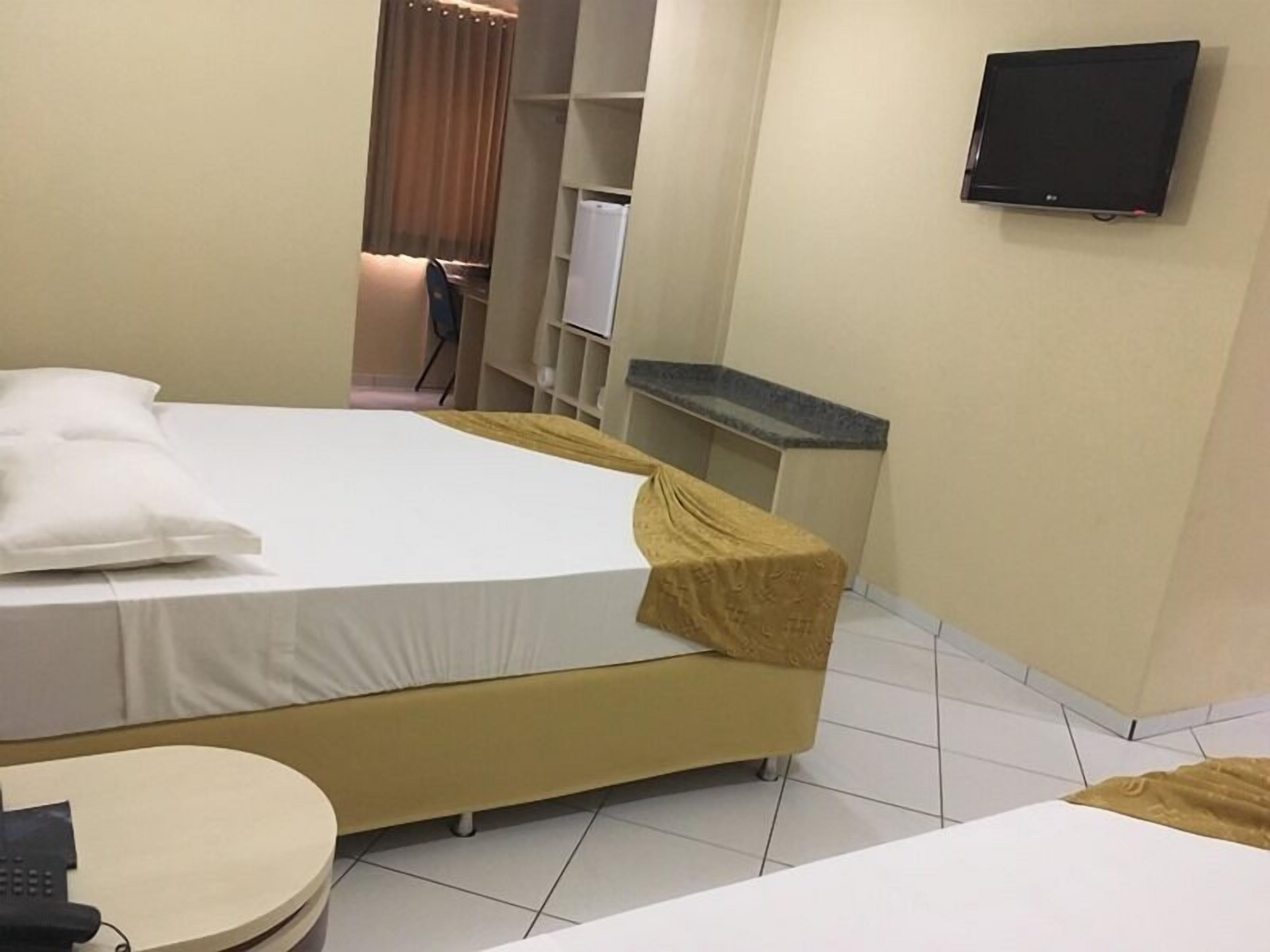 A hotel room with a bed, a small round table, a television mounted on the wall, and a desk with a computer.