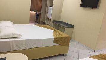 A hotel room with a bed, a small round table, a television mounted on the wall, and a desk with a computer.
