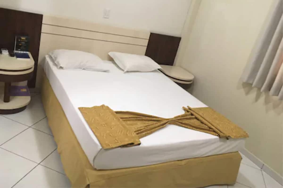 A hotel room with a bed, two bedside tables, a nightstand, and a window with curtains.