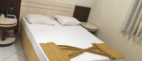 A hotel room with a bed, two bedside tables, a nightstand, and a window with curtains.