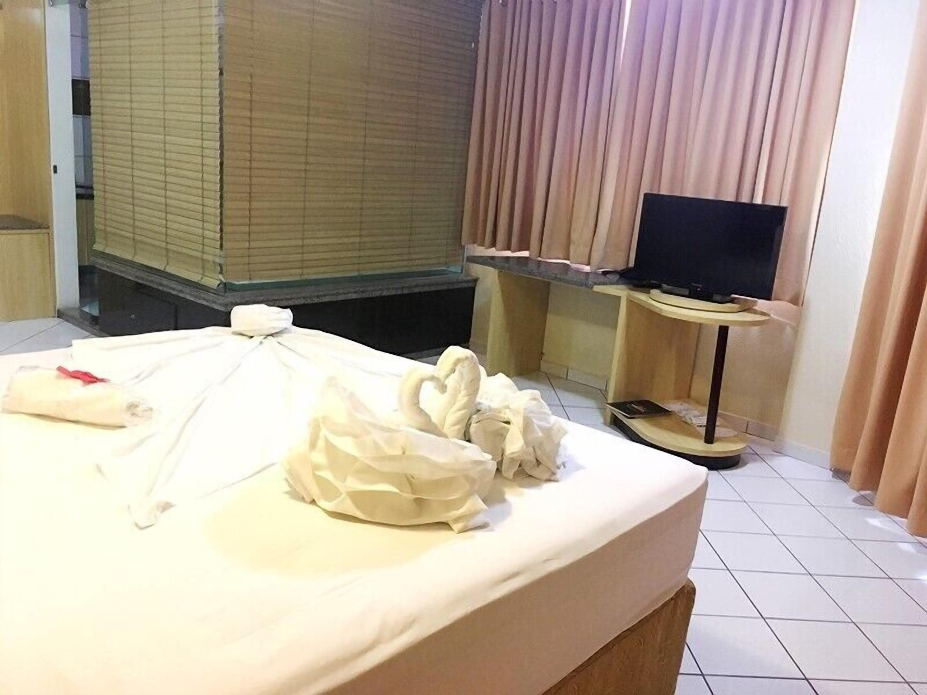 A hotel room with a bed, a television on a stand, and a window with curtains.