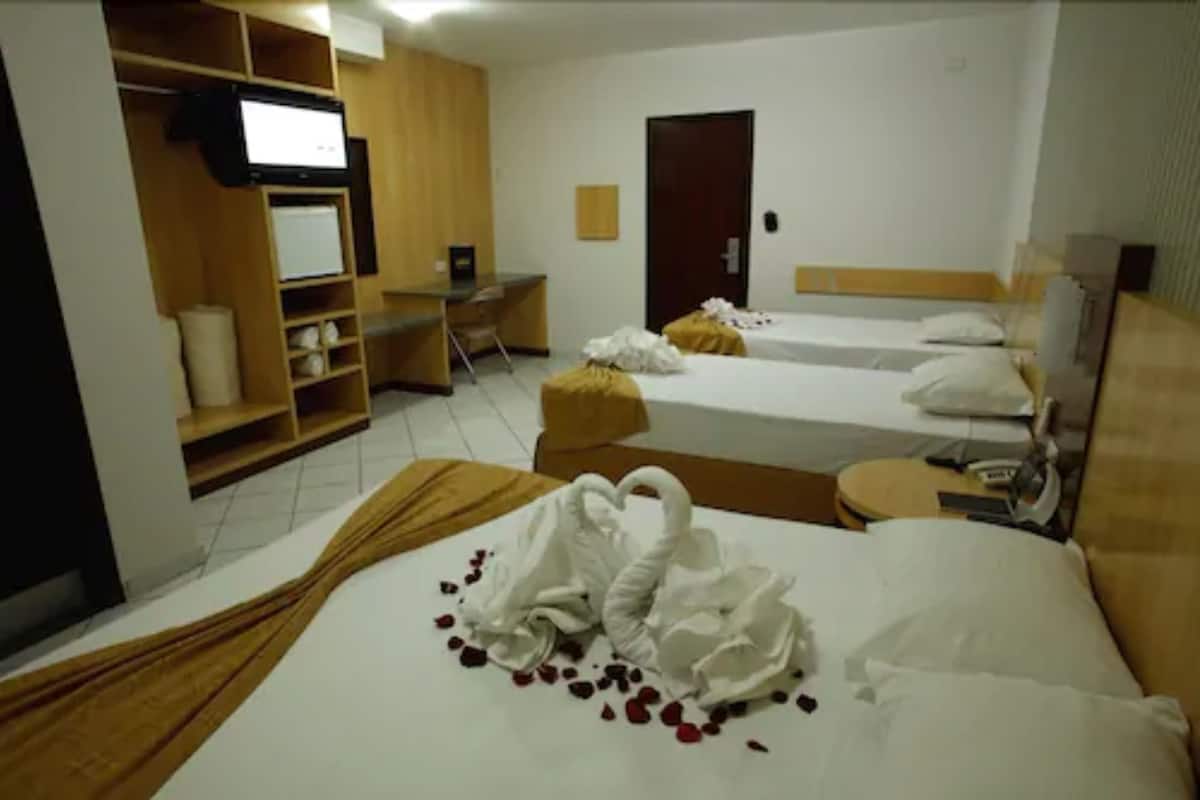 A hotel room with two beds, a desk, a wardrobe, and a television.
