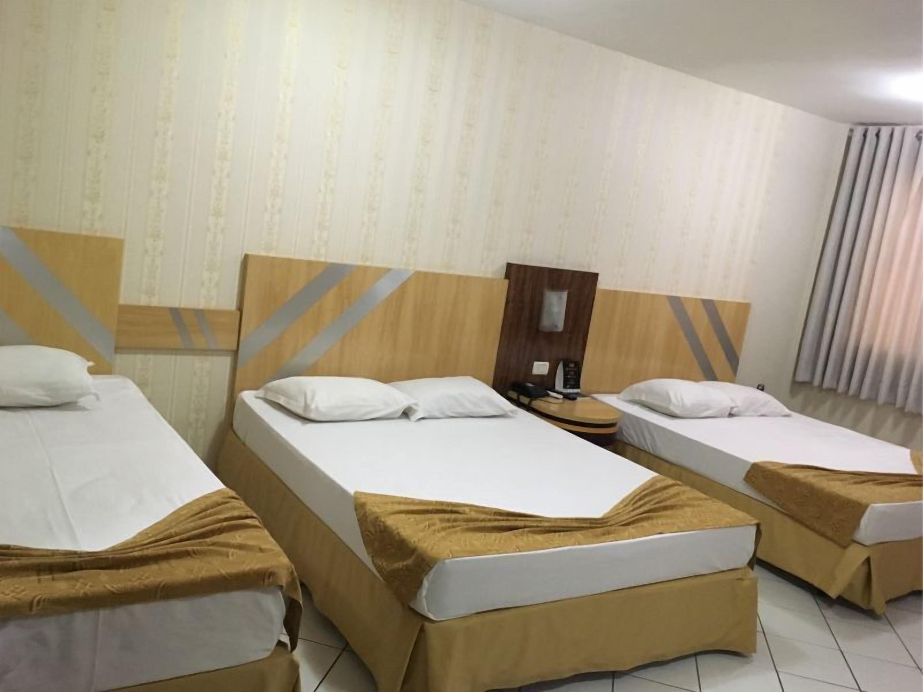 Una habitación de hotel con tres camas individuales, cada una con cabecero de madera y colcha marrón.