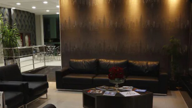 A modern living room with a black leather sofa, a coffee table with magazines, and a cityscape mural on the wall. - King Konfort Hotel (Maringá)