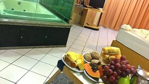 A room with a bathtub, a small table with snacks, a TV, and curtains. - King Konfort Hotel (Maringá)