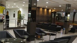 A modern lounge area with black sofas, small tables, and a large mirror. - King Konfort Hotel (Maringá)