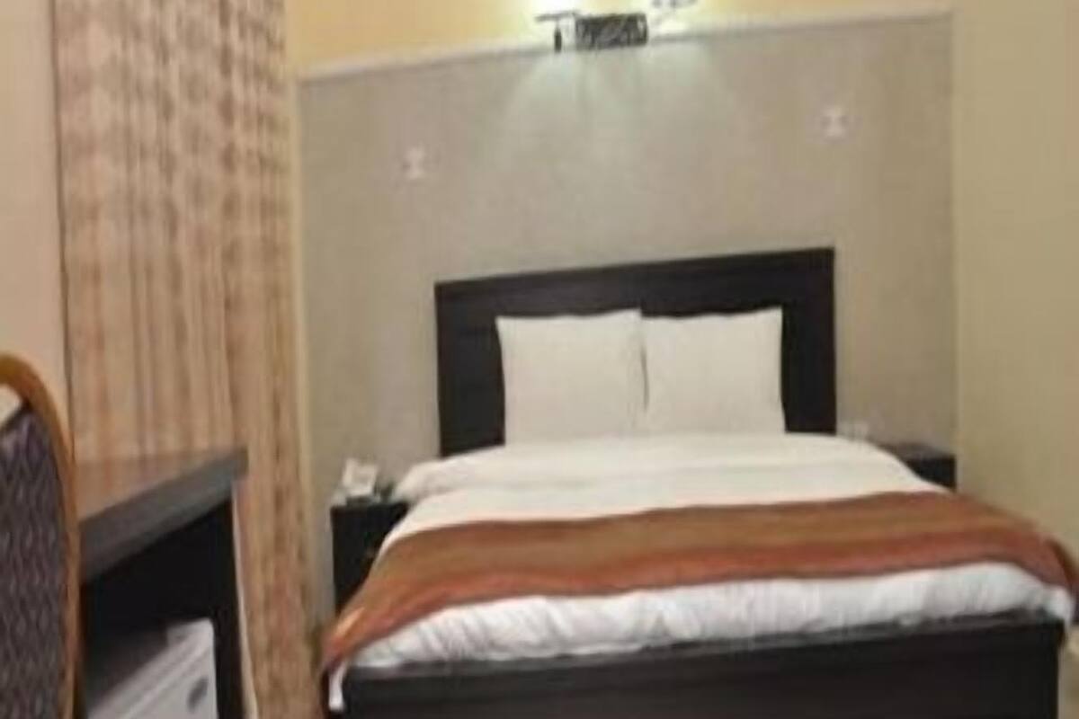 A hotel room with a single bed, a nightstand, a desk with a chair, and a small refrigerator.