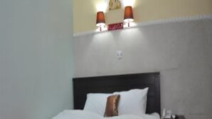 A bedroom with a bed, a nightstand, and wall-mounted lamps. - Grand Capital Hotel (Akure)