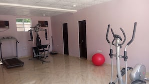 Een fitnessruimte met trainingsapparatuur, waaronder een loopband, hometrainer en een vastzetfiets.